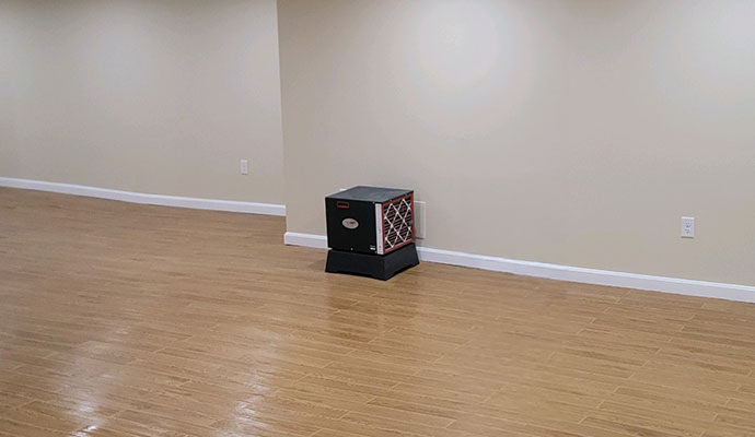 Basement dehumidifier unit running on wood flooring in a finished basement