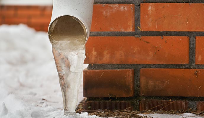 Frozen discharge line from gutter system near brick wall