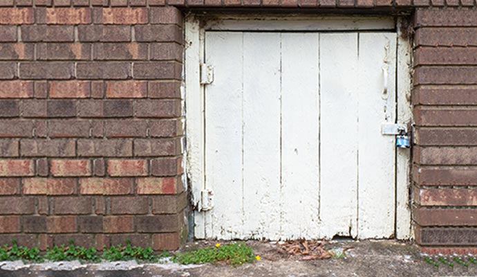 Old crawl space access panel positioned next to a brick wall.