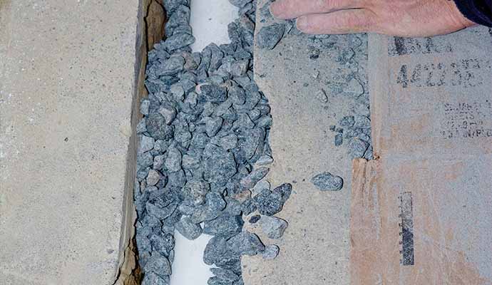 Professional installing interior french drain pipe gravel