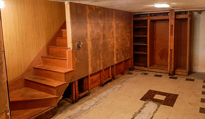 Unfinished basement wooden stairs and damaged floor tiles